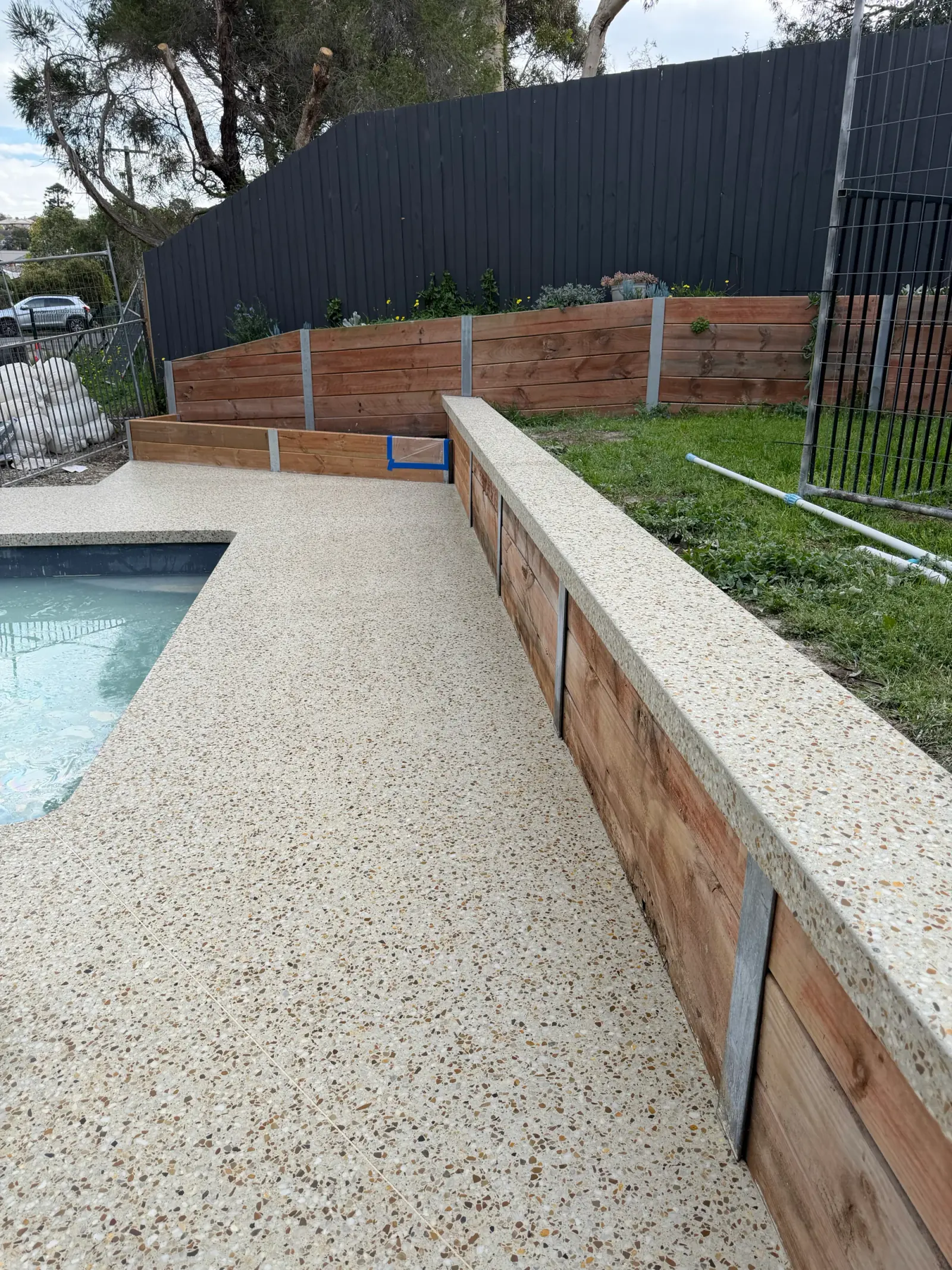 Exposed-stone Pavilion concrete along a pool edge and beside a timber retaining wall in Highton